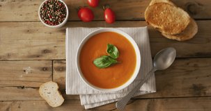 Video of cream tomato soup in bowl on wooden table with tomato and bread. American cuisine, meal, food and cooking concept.