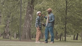 Full length slowmo portrait of cheerful African American father and his teenage son embracing each other and smiling at camera while standing on sports field in park during baseball training - Powered by Shutterstock - Get 15% off with code: PIKWIZARD15