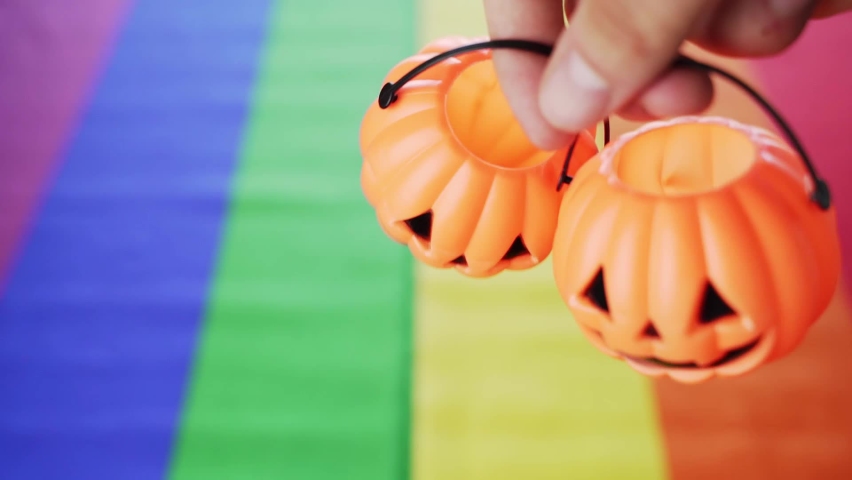 Two Halloween pumpkin head baskets hanging by fingers with lgbt pride flag