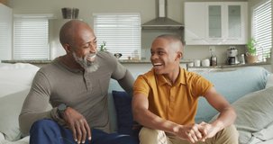 Video of happy african american father and son sitting on sofa and laughing. Family, spending quality time together at home.
