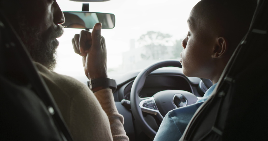 Video of happy african american father learning son how to drive a car. Family, driver lessons and spending quality time together.