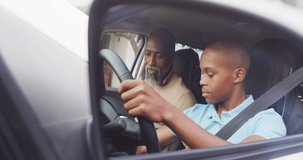 Video of focused african american father learning son how to drive a car. Family, driver lessons and spending quality time together.