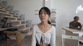 Asian woman waves hello to friend via video call sitting at desk in office. Brunette lady turns to man with long hair to talk from POV to third party