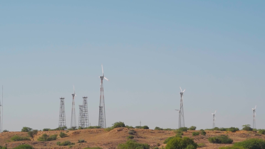 Windmills in a windfarm as seen from the Bada Bagh at Jaisalmer in Rajasthan, India. Wind Power Turbines Generating Clean Renewable Energy for Sustainable Development. Concept of using clean energy.  | Shutterstock HD Video #1094553027