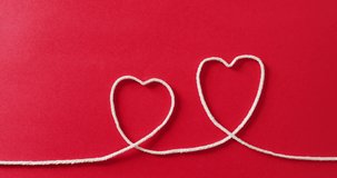 Video of close up of hearts of string on red background. Clothing, textile and copy space concept.