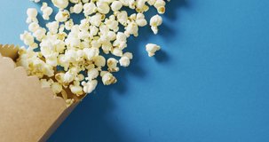 Video of close up of box of popcorn on blue background. Food, party and copy space concept.