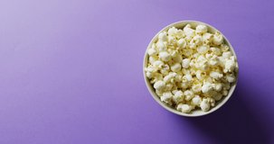 Video of close up of popcorn on purple background. Food, party and copy space concept.