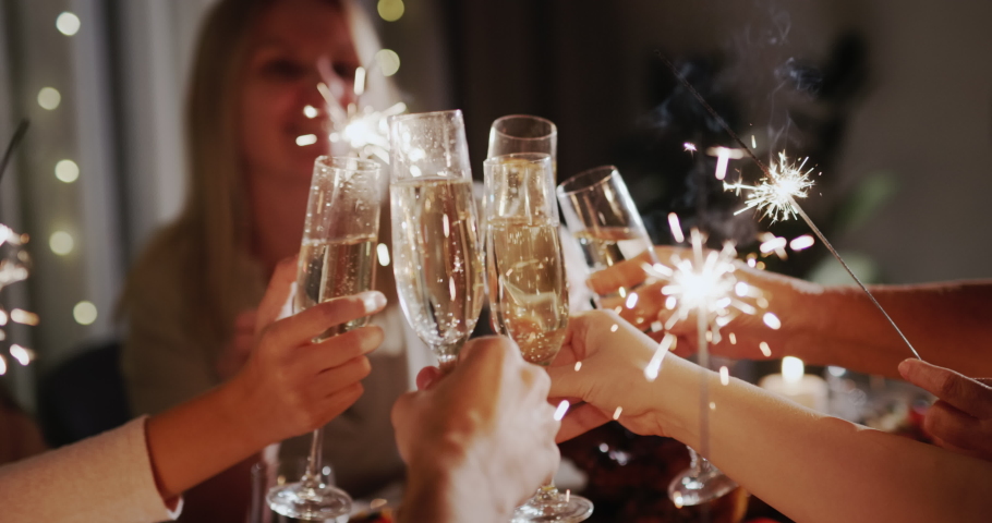 A group of people at the festive table clink glasses, holding sparklers in their hands. New Year's Eve Royalty-Free Stock Footage #1094555867