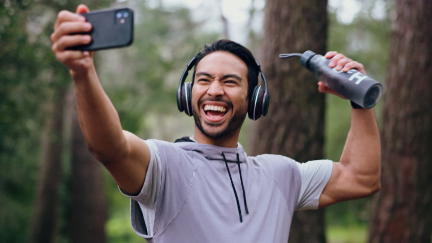Fitness man, selfie and headphones during forest workout listening to music and taking pictures for social media of influencer content. Happy asian male out for a run, training and exercise in nature Royalty-Free Stock Footage #1094557001