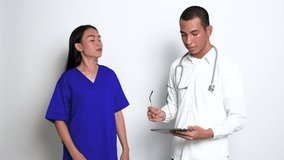 Video Footage From a Young Male Doctor Checking on a Report at a Tablet While Discussing it to a Nurse on His Side While the Nurse Nodding Continuously at a White Background