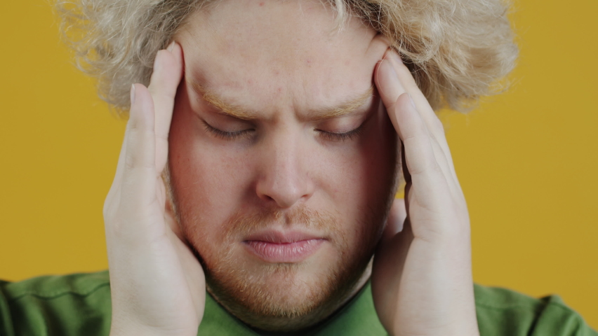 Close-up portrait of stressed young man massaging head suffering from headache on yellow background. Health problems and people concept. Royalty-Free Stock Footage #1094561127
