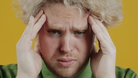 Close-up portrait of stressed young man massaging head suffering from headache on yellow background. Health problems and people concept. - Powered by Shutterstock - Get 15% off with code: PIKWIZARD15