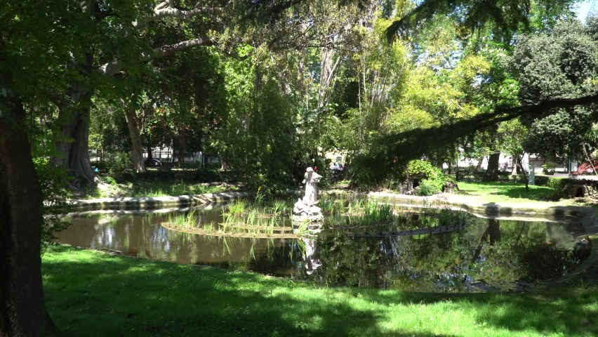 A beautiful white statue of a woman decorates the center of a pond in a park in inner city Lisbon in Portugal.