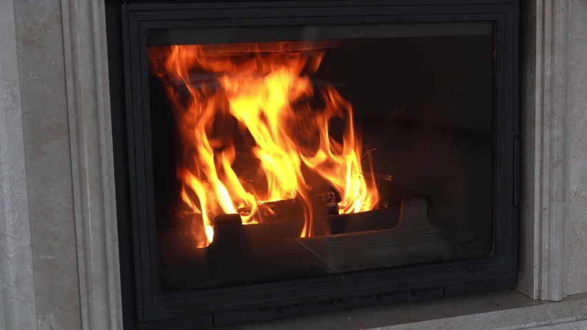 Stylish cast iron fireplace with fire in home interior lined with marble stone. Modern stove to decorate and heat house with the fire burning wood. Orange tongues of flame dance behind fireproof glass Royalty-Free Stock Footage #1094567913