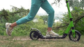 A close-up of the legs of a girl riding a scooter. Happy family walks in the park. Slow motion video of feet pushing off the ground. High quality 4k footage