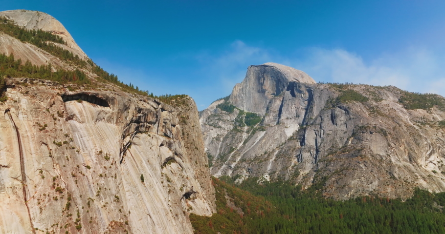 Slow motion approach to the cliffs in Yosemite National Park, California, USA. Pine tree wood growing at the foot of mountain. Royalty-Free Stock Footage #1094572951