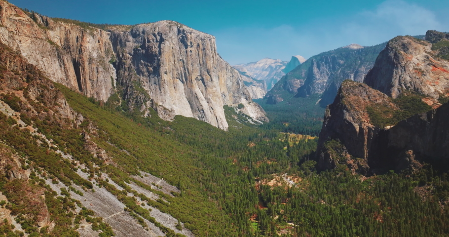 Bright sunny day scenery in Yosemite National Park, California, USA. Amazing cliff mountains with green forests at its foot. Aerial view. Royalty-Free Stock Footage #1094572985