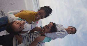 Vertical video of happy biracial family embracing on sunny beach. healthy, active time beach holiday.