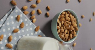 Vertical video of a bowl of almonds and bottle of milk on lilac background. healthy snack food, diet and nutrition.