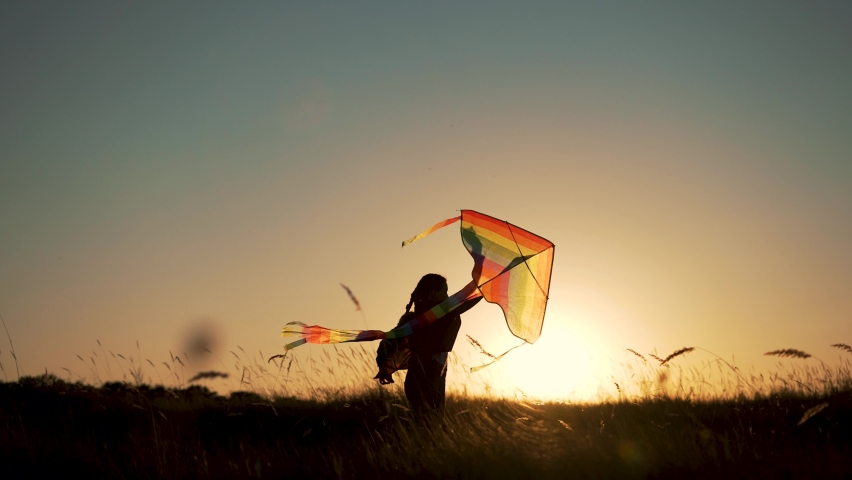 Happy child. Girl with flying kite in park. Child runs at sunset on grass in park. Silhouette of girl with flying kite. Child launches flying kite into sky in the wind. Silhouette of child in meadow | Shutterstock HD Video #1094574413