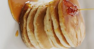 Vertical video of maple syrup pouring onto stack of american style pancakes. home cooking sweet treat, food, flavour and nutrition.