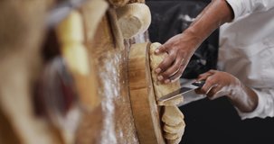 Vertical video of midsection of african american baker slicing loaf of white bread on chopping block. healthy food, diet and nutrition.