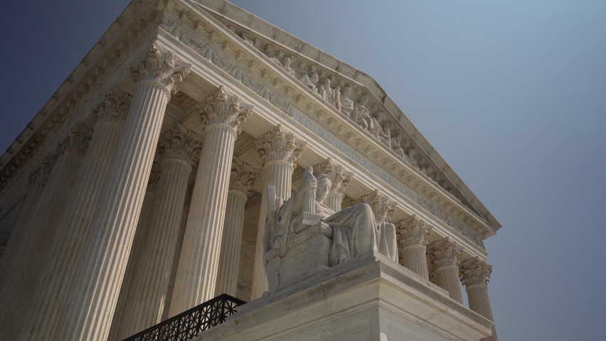 Turning view of facade of US Supreme Court building with Contemplation of Justice sculpture in front on a sunny summer day.