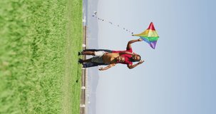 Vertical video of happy african american father with son flying kite. spending free time during holiday.