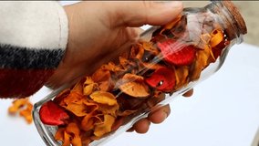 A small video clip of a hand with a decorative glass bottle with its cork stopper, inside dried flower petals in autumn colors