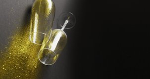 Vertical video of two fallen champagne flute glasses spilling gold glitter. New year's eve party and celebration concept.