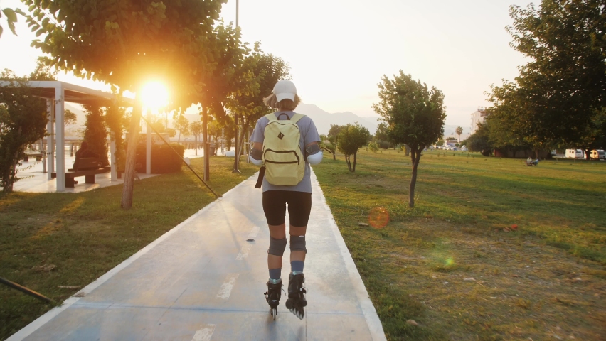 Young pretty woman rolling skating at sunset in the city park.