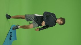Vertical Footage. Motivated Sporty Mexican Man Doing Breathing Exercises Raising Legs Up and Down against Green Screen Background. The Mat and Dumbells are Lying near Him. Domestic Physical Jerks.