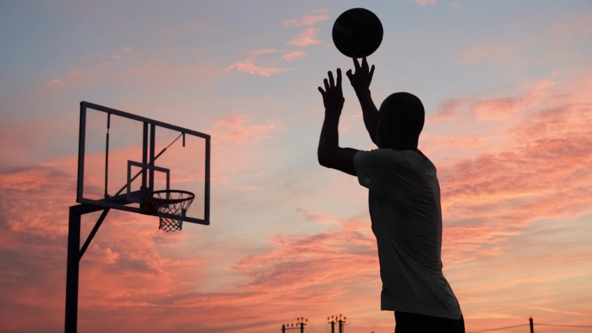 4k video Silhouettes of basketball players at the beautiful sunset. Amazing cinematic sport shoot. Two male playing street ball outside. Royalty-Free Stock Footage #1094590221