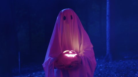 Стоковое видео: Portrait child ghost in the hands of an orange glowing jack pumpkin walks forest night misty forest with forest moonlight. Halloween holiday, terrible horror ghost.