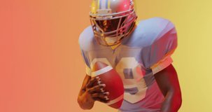 Video of african american american football player with ball over yellow to orange background. American football, sports and competition concept.
