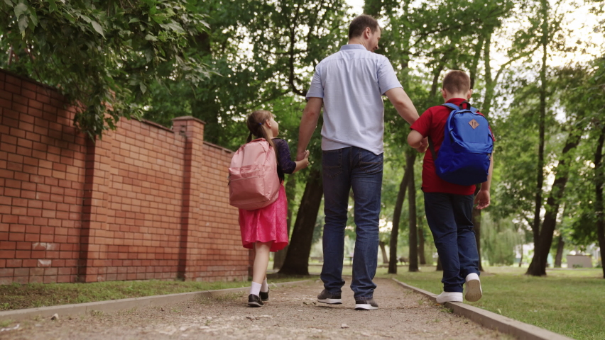 happy family. father holding hands children school. little kids school bags go school holding dad hand. concept happy family outdoors. schoolchildren with parent view from back. children education Royalty-Free Stock Footage #1094597053