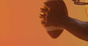 Video of african american american football player with ball over orange background. American football, sports and competition concept.