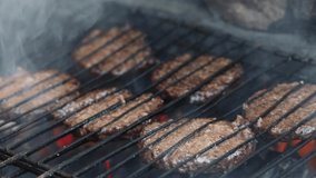 Grilling meat cutlets for burgers. Fast food or street food. Steel grill grate, cutlet in the smoke. Selected focus, macro close-up video footage