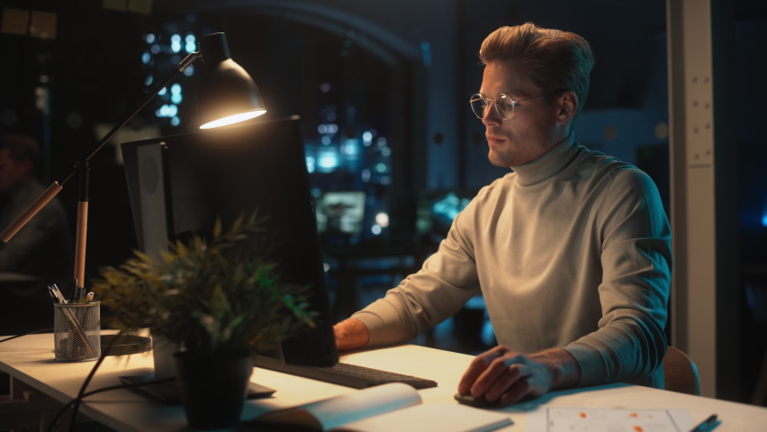 Portrait of a Stylish Male Working on Desktop Computer in a Company Office in the Evening. Young Manager Browsing Internet, Shopping Online and Reading Social Media Posts from Friends and Colleagues.