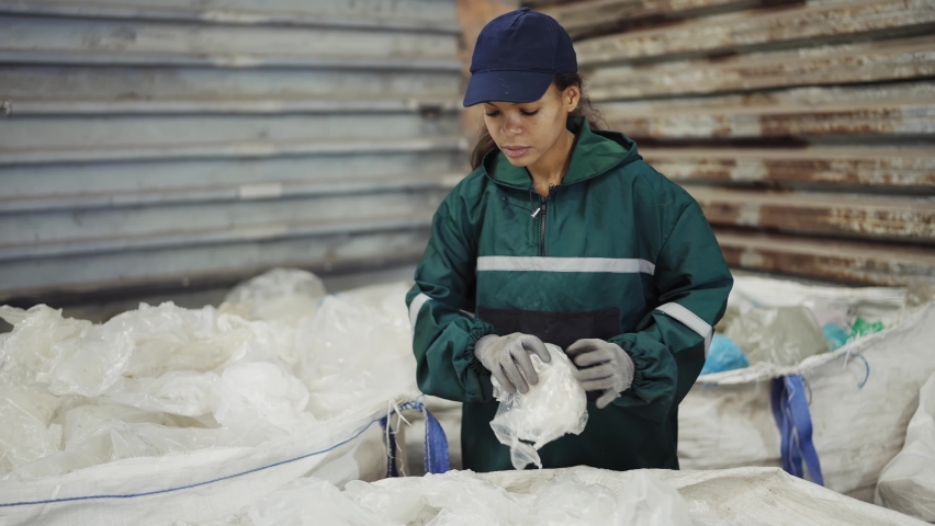 An African-American woman in a special uniform sorts polyethylene at a waste recycling plant. Processing of raw materials, recycling. Pollution control | Shutterstock HD Video #1094605307