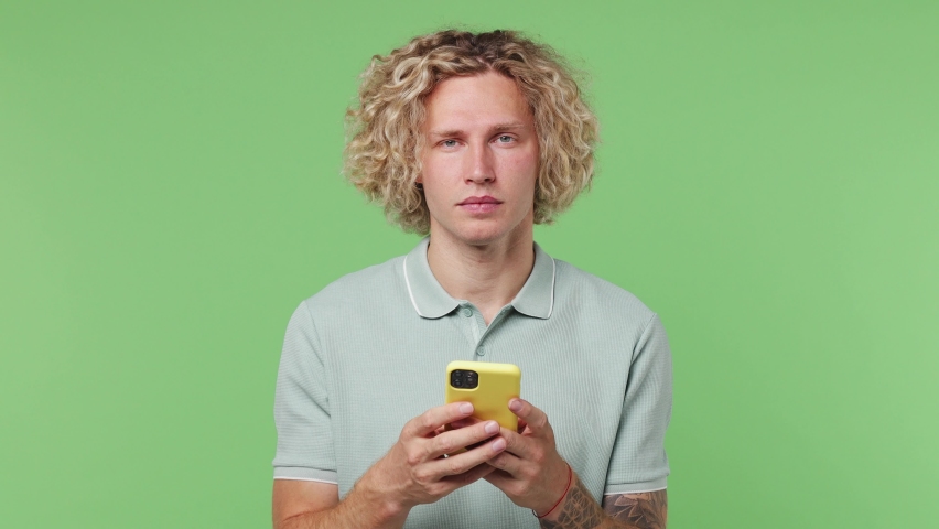 Young happy excited blond man he wear blue t-shirt hold use mobile cell phone typing say wow yes just found out great big win news doing winner gesture isolated on plain pastel light green background