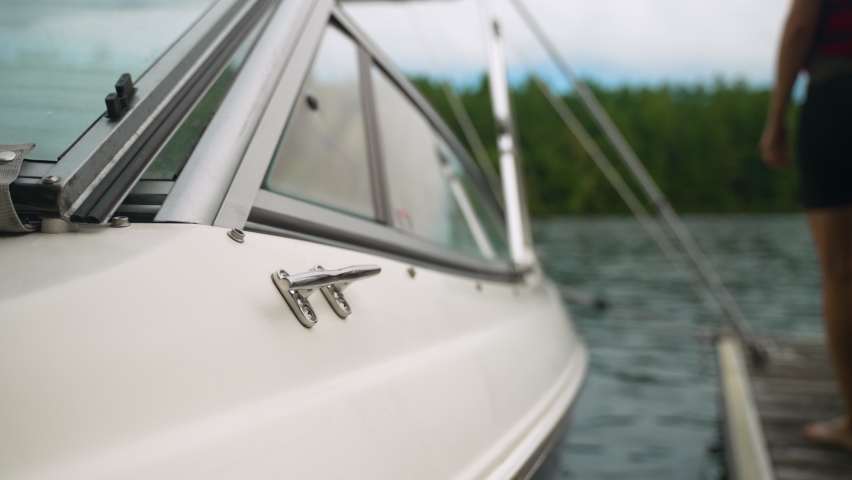 Defocused view of a woman wearing a life jacket as she steps off of a dock and into a boat. Slow motion.