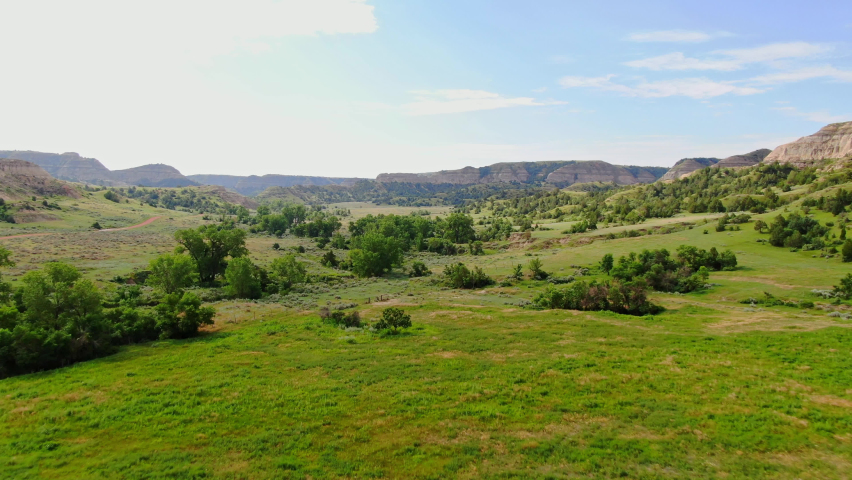 Aerial Rising Up Panoramic View of Vast Wild Green Grassland Field Land in Grassy Butte Region North Dakota, Plain Prairie Rural Area with Vegetation Trees and Mountains in Horizon, Summer Landscape