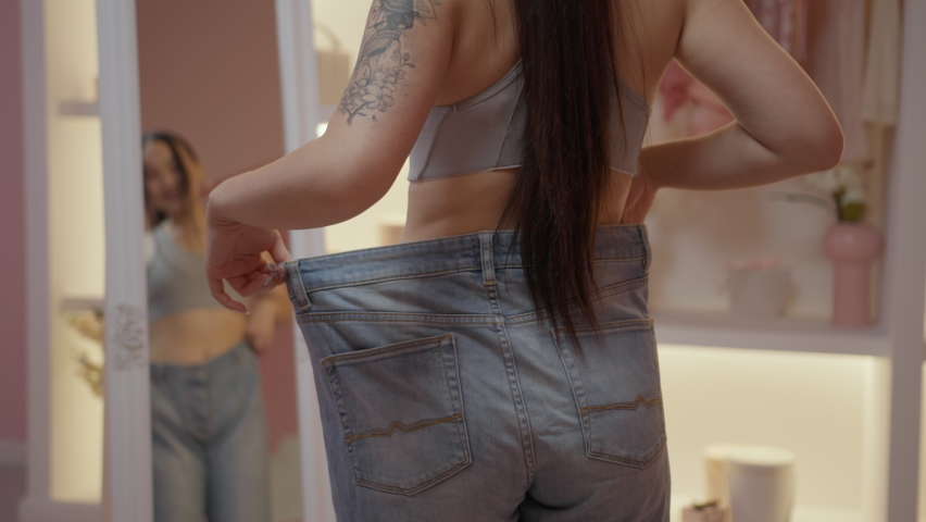 Back of Asian woman wearing oversized jeans looking at the mirror. Focus on woman in big jeans. | Shutterstock HD Video #1094610967