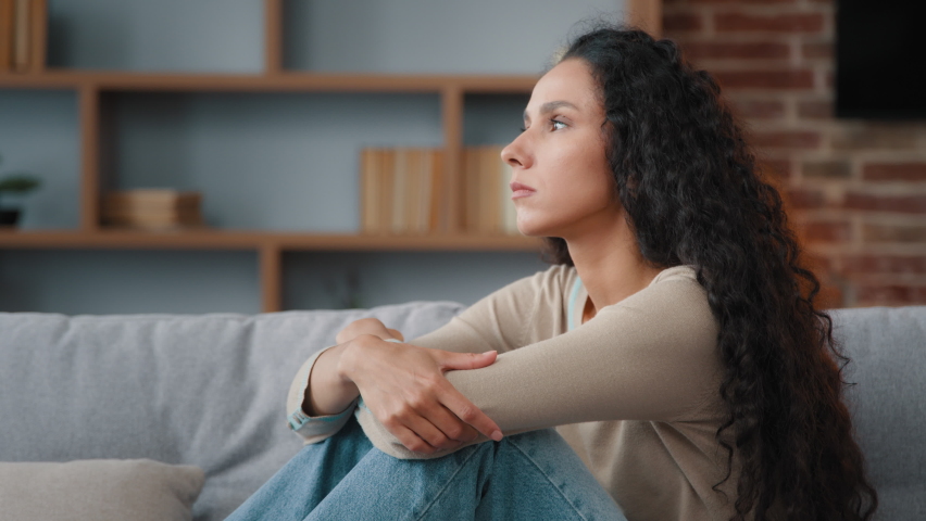 Pensive sad upset worried annoyed Hispanic Latino Caucasian woman 30s lady sitting on couch feeling sadness worry about problem stress trouble bad unwell headache unwanted pregnant bored mood indoors | Shutterstock HD Video #1094612347