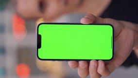 Close up of Smartphone with Green Mock-up Screen in man's hand on urban background. Vertical Video
