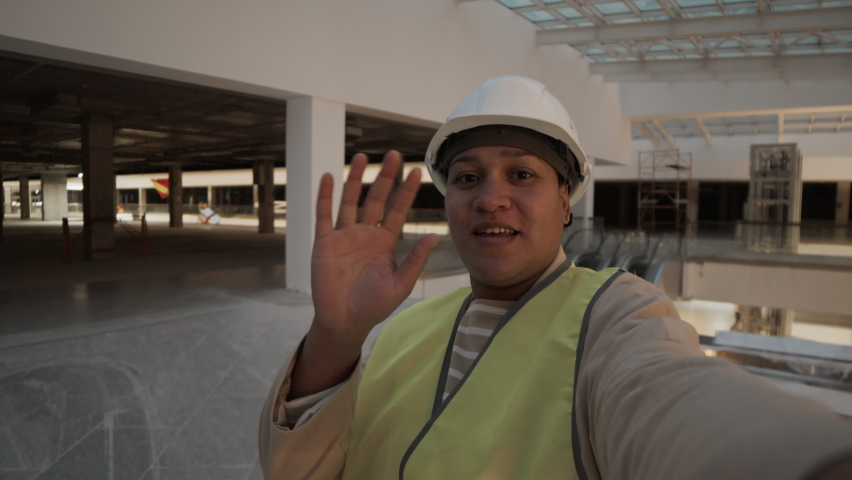 Handheld medium close-up POV of cheerful brown-eyed Biracial female construction worker in white hard hat talking, looking on camera, filming video blog in building under construction Royalty-Free Stock Footage #1094613791