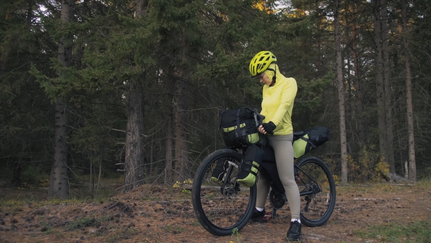 The woman travel on mixed terrain cycle touring with bike bikepacking outdoor. The traveler journey with bicycle bags. Stylish bikepacking, bike, sportswear in green black colors. Magic forest park.