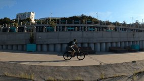 Cinematic FPV video shot of male cyclist wearing sunglasses and carrying backpack riding mountain bicycle along city promenade in early morning sunrise. Tracking shot in slow motion.