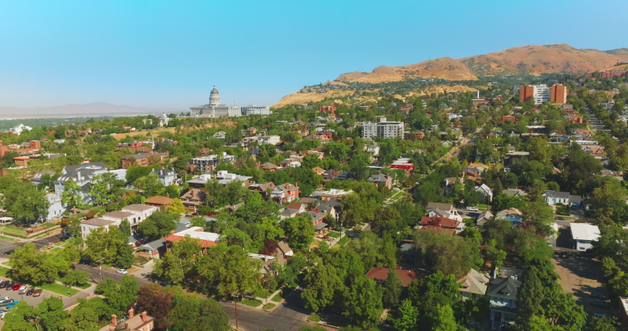 Beautiful sunny city built near the bare mountain. Magnificent State Capitol Building at the foot of rock. Salt Lake City panorama on clear summer day.